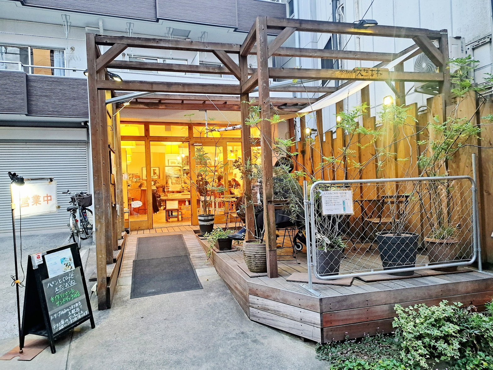夜間の外観、木製パーゴラの奥に暖色照明の店内が見え、黒板看板と営業中の表示が路上に立つ